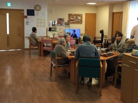テレビのある食堂で、テーブルを囲んで食事をしている入居者様たち