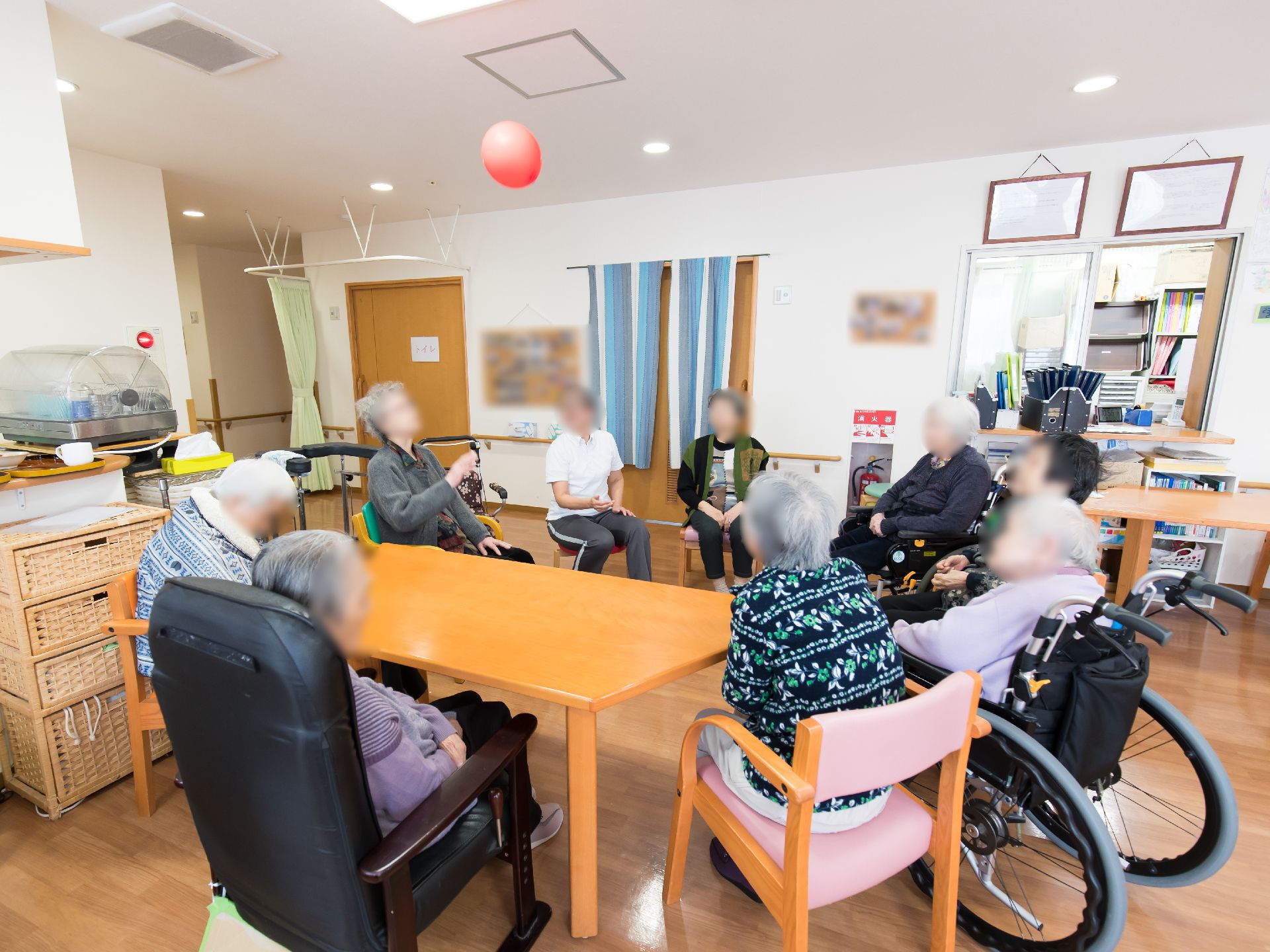 消火設備の整った共有スペースでは入居者様、皆さまが集って円陣になり風船ゲームのレクリエーションを行っている。