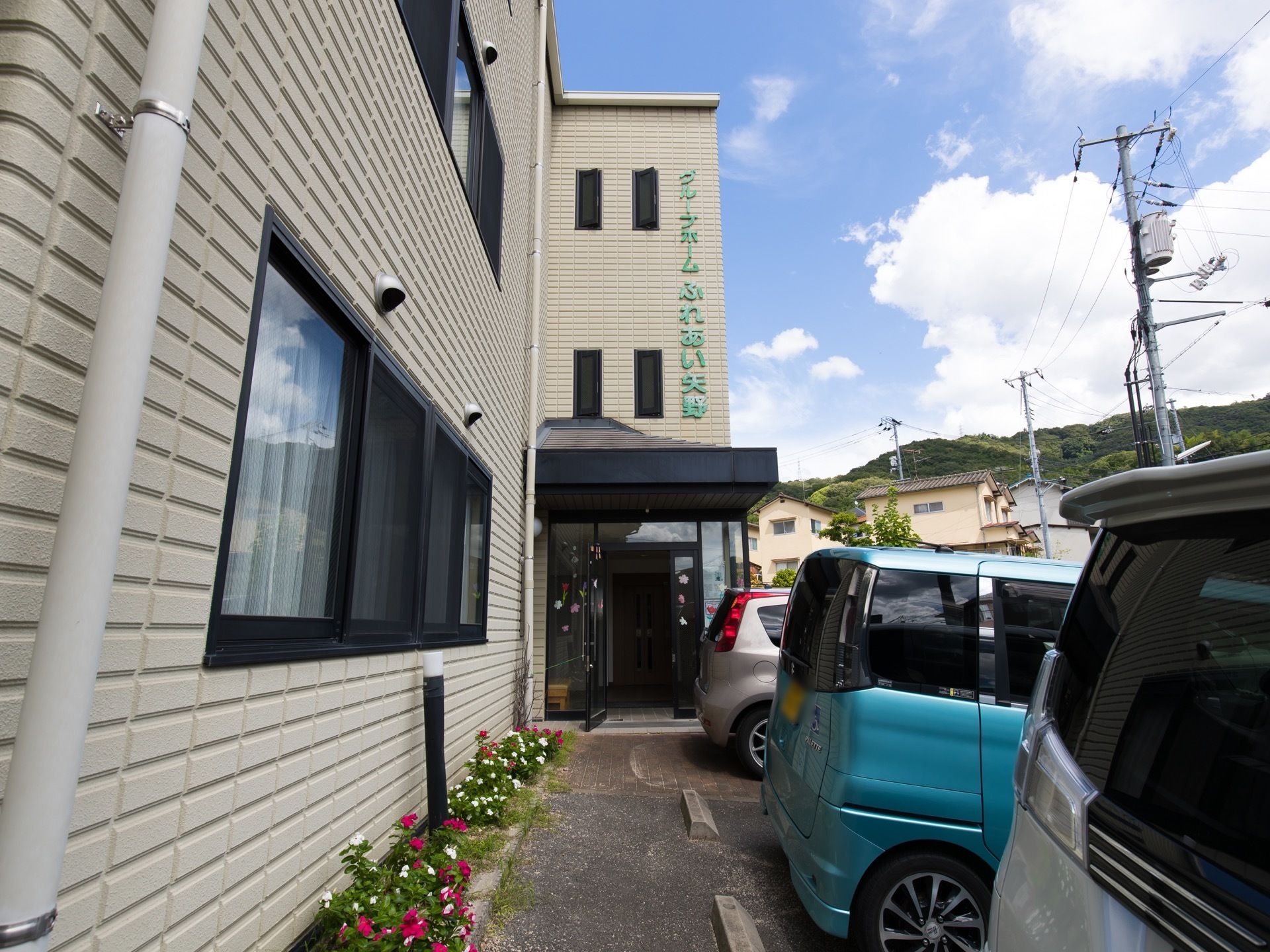 エントランスは玄関扉までバリアフリーになっている。建物に沿って花壇が設けられている。駐車場が建物前にある。
