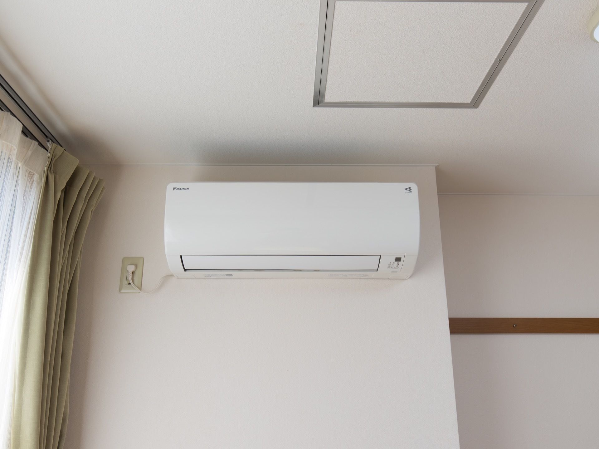 居室には、エアコンが完備されている。左横に設けられた窓には、レースと緑色のカーテンが掛けられている。