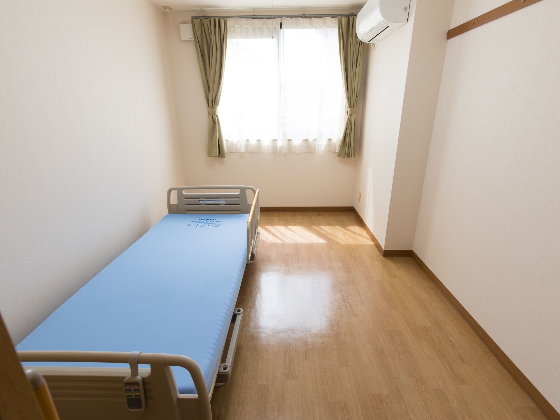 個室の居室である。エアコンや介護ベッドが完備されており、明るい自然光が差し込む窓が設けられている。扉は引き戸になっている。