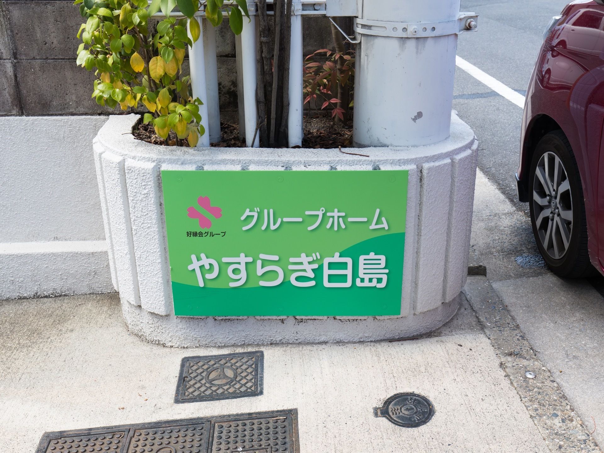 道路に面したコンクリートの側面に、施設の看板が貼られている。背景色はグリーン、文字はホワイトで描かれている。