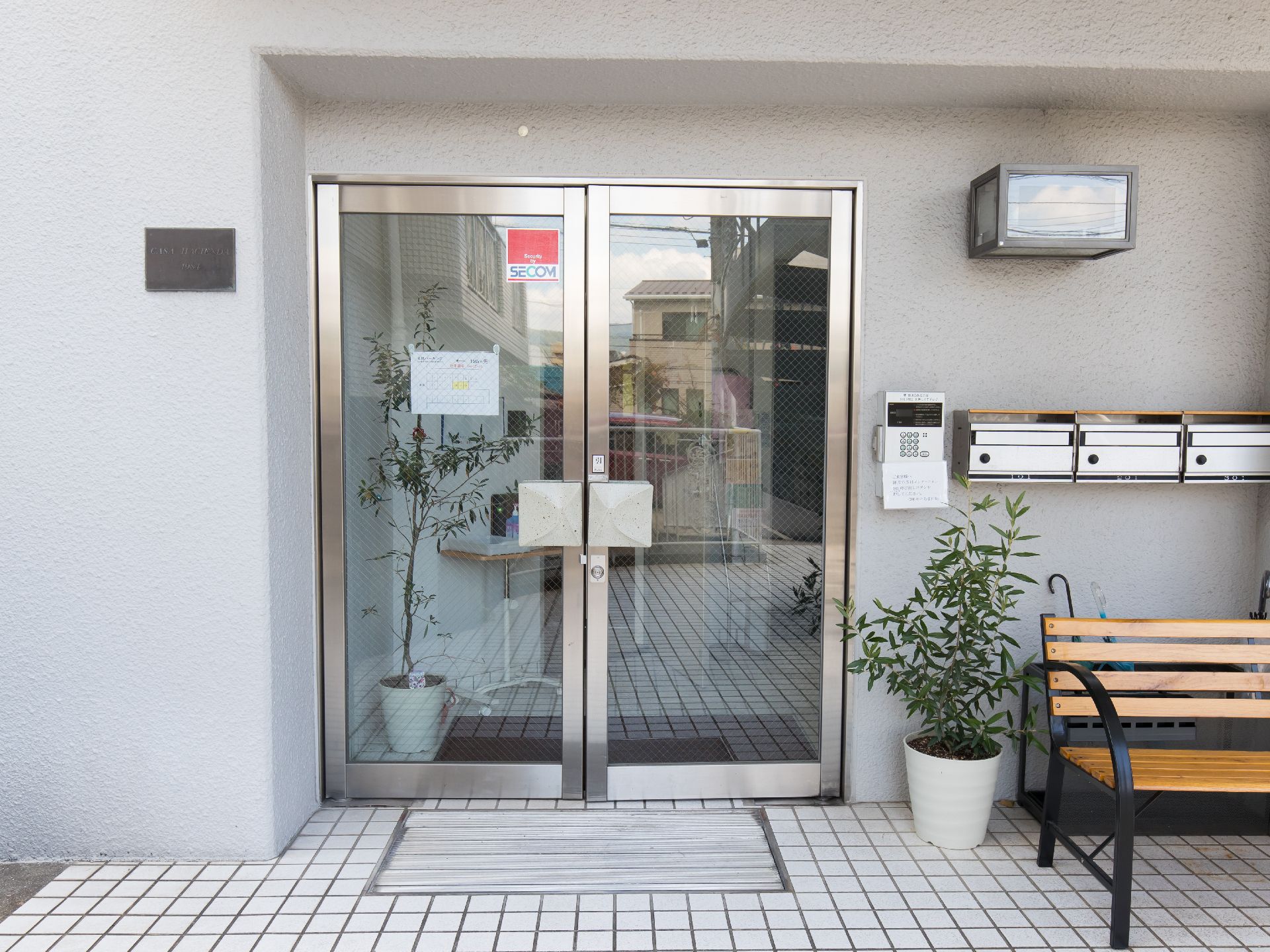 観葉植物とポストが三つある、両開きのガラス扉の玄関