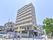 左側には3台の自動販売機が置かれている。右側には9階建ての建物がある。3階以上にはベランダが付いている。外壁はクリーム色が使われている。