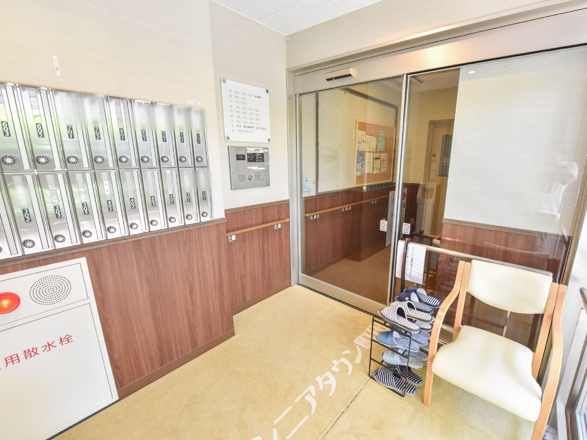 右側には室内に入るための自動ドアがあり、そばには手すりが付いている。床には施設名が書かれたマットが敷かれている。