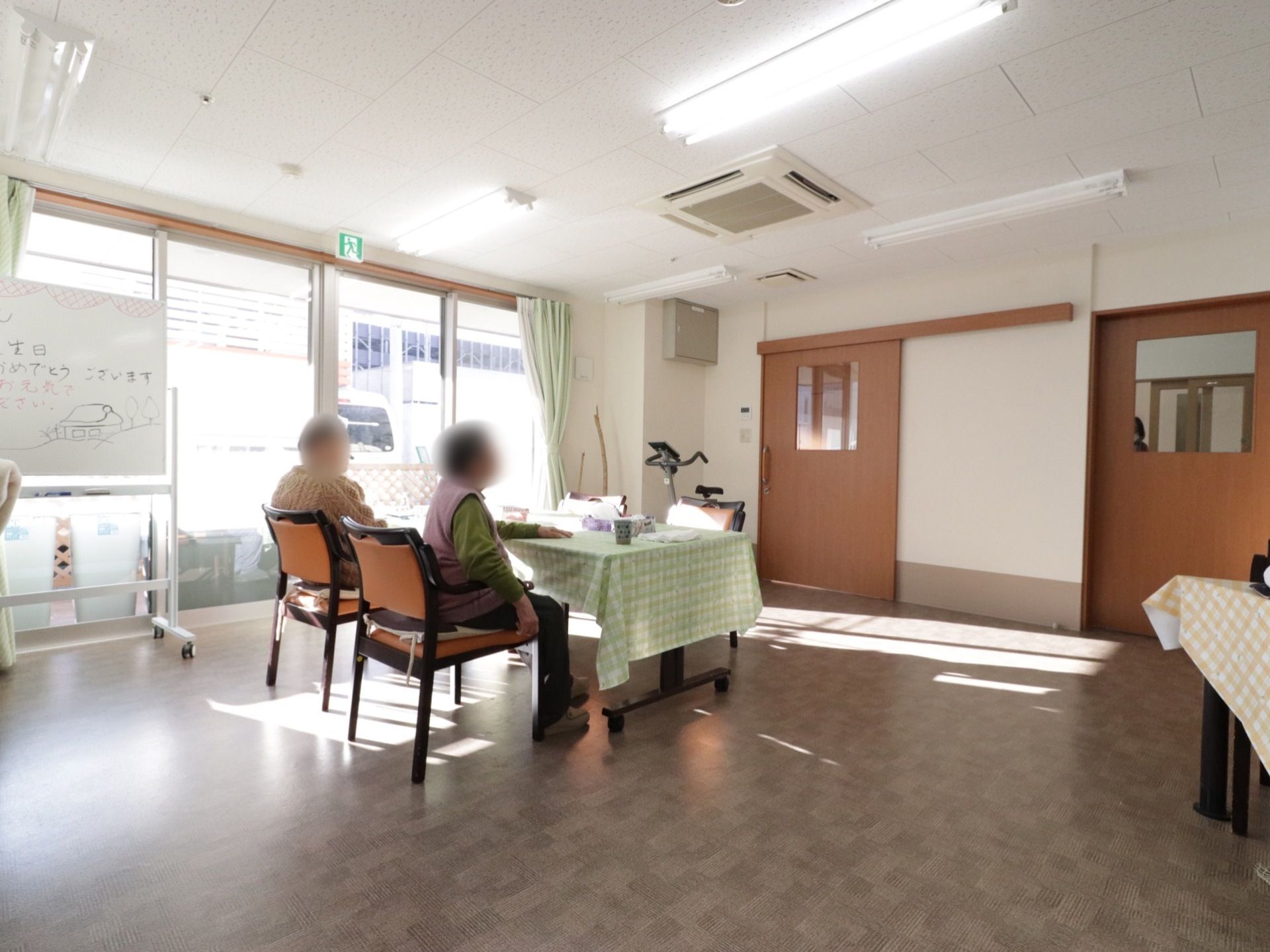 広々としたリビングの窓のそばにメッセージが書かれたホワイトボードが置いてある。上部がガラスになった扉が２つある。