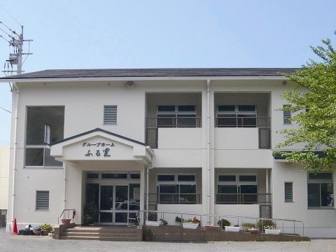 スロープに沿ってプランターの花が咲く、シンボルツリーのある建物