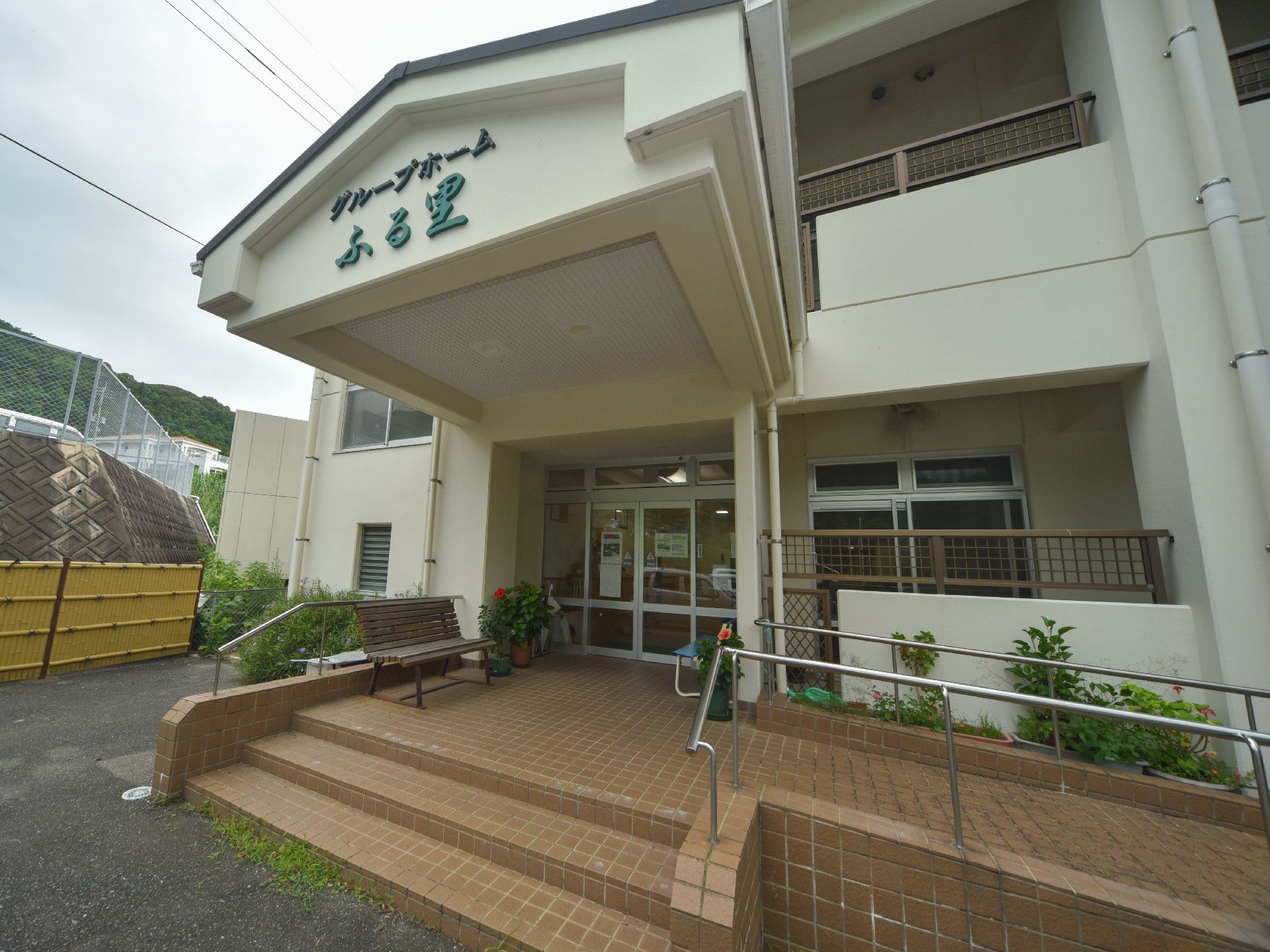 ポーチ屋根が大きく、前面に施設の名称が書かれている。ポーチにはベンチや花の植えられた植木鉢が置かれている。
