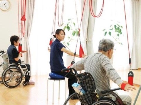 窓辺に設置された器具で、車椅子に座ったまま運動をするスタッフと入居者様