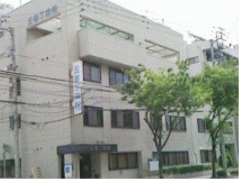 病院の建物内に施設が入っている。玄関前にはひさしがあり、ひさしや建物の壁に病院名が掲げられている。歩道には木が植わっている。