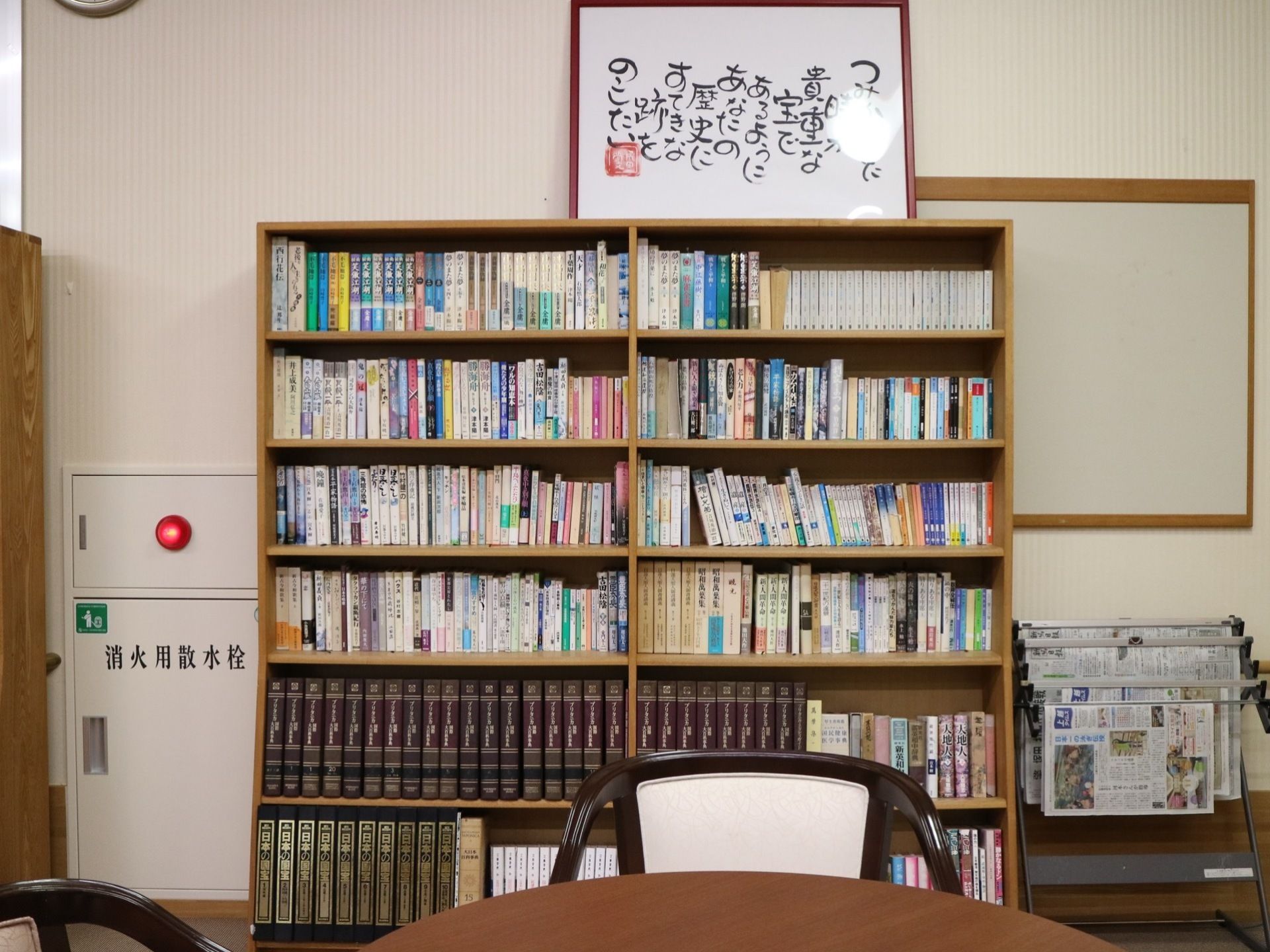 大きな書棚に小説や歴史書などたくさんの書籍が並べられている。その隣には数種類の新聞が掛けられている。