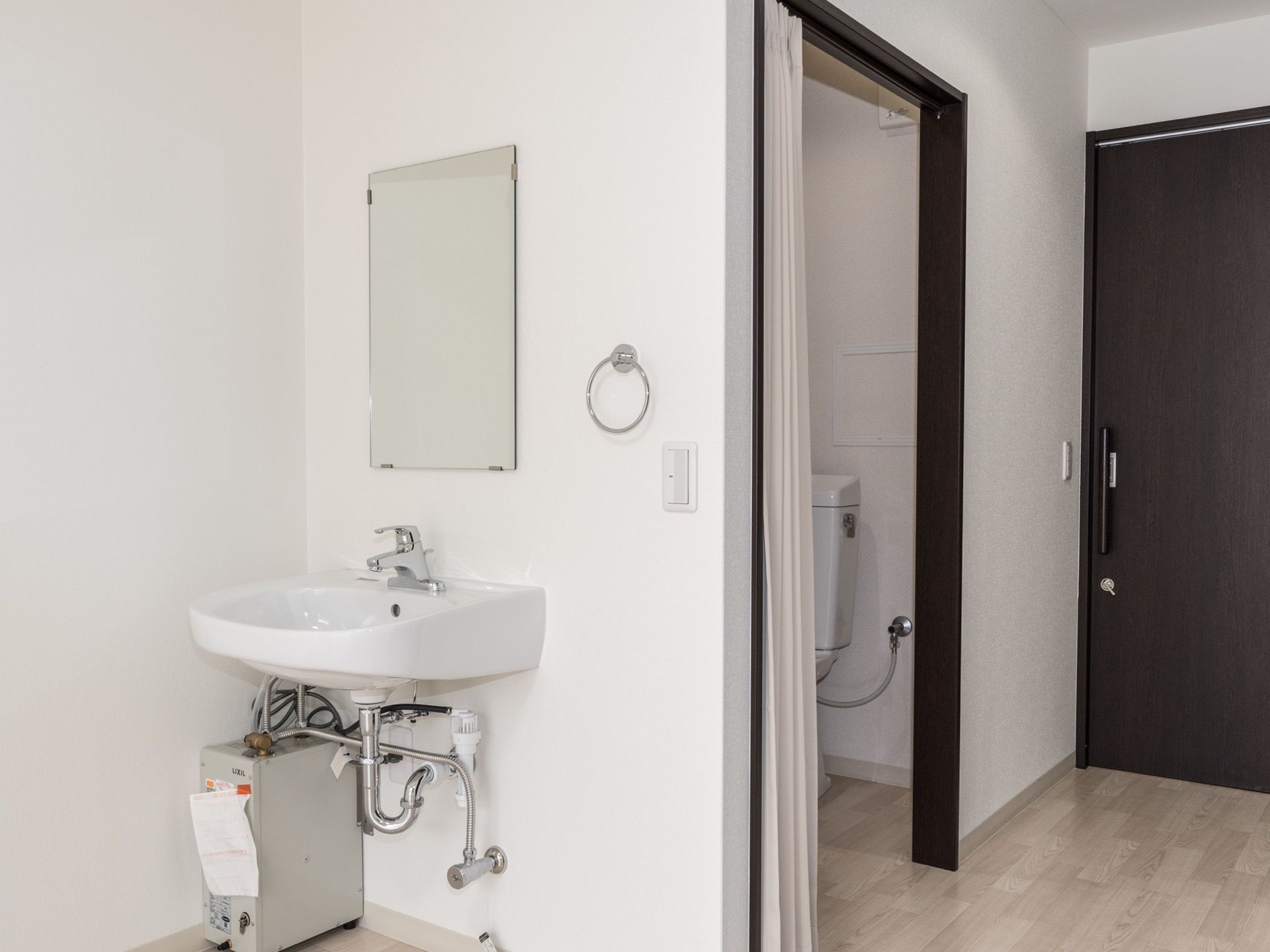 カーテンで区切られたトイレがある。洗面所が設けられている。居室の扉はスライド式になっている。床はフローリングで段差がない。