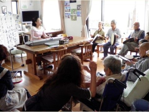 キーボ－ドを弾く女性の周りに集まって演奏をしている入居者様たち