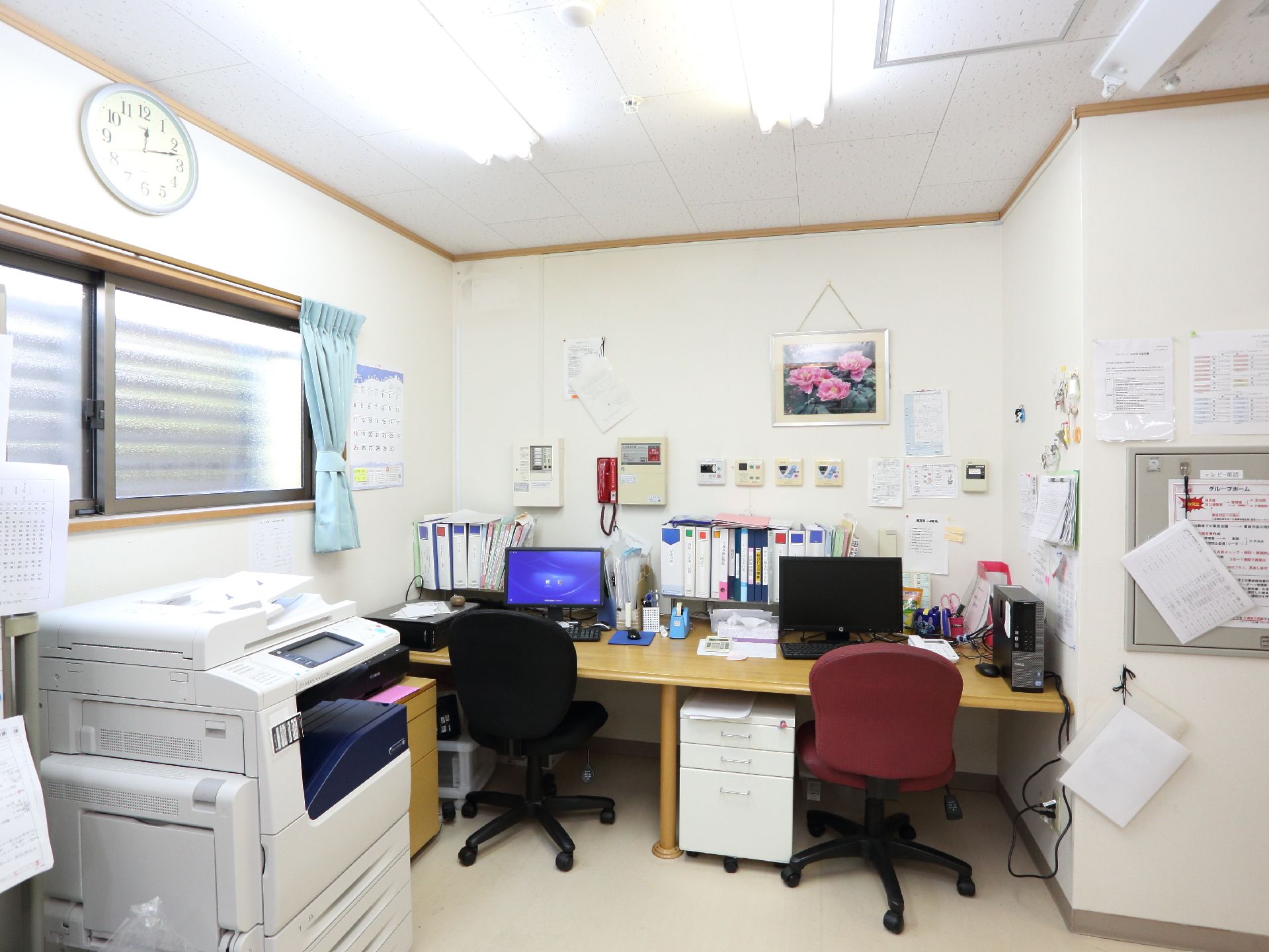 事務所の中には、デスクが2つあり、それぞれパソコンが置かれている。書類のファイルも置いてある。また、コピー機が設置されている。