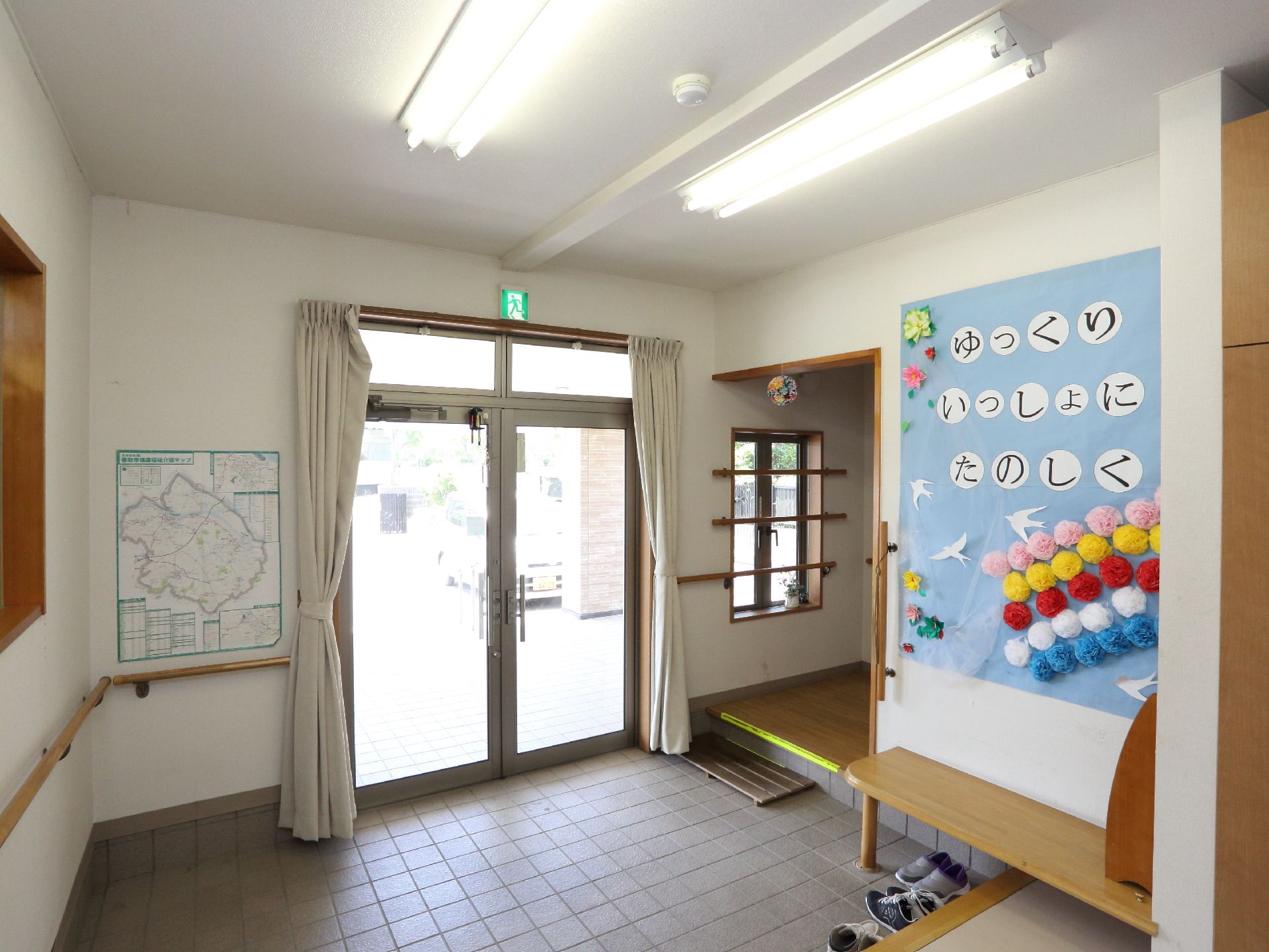 明るいエントランスである。腰壁には手摺が設置してある。出入口は間口の広い両開きドアになっており車椅子利用者でも通過可能である。