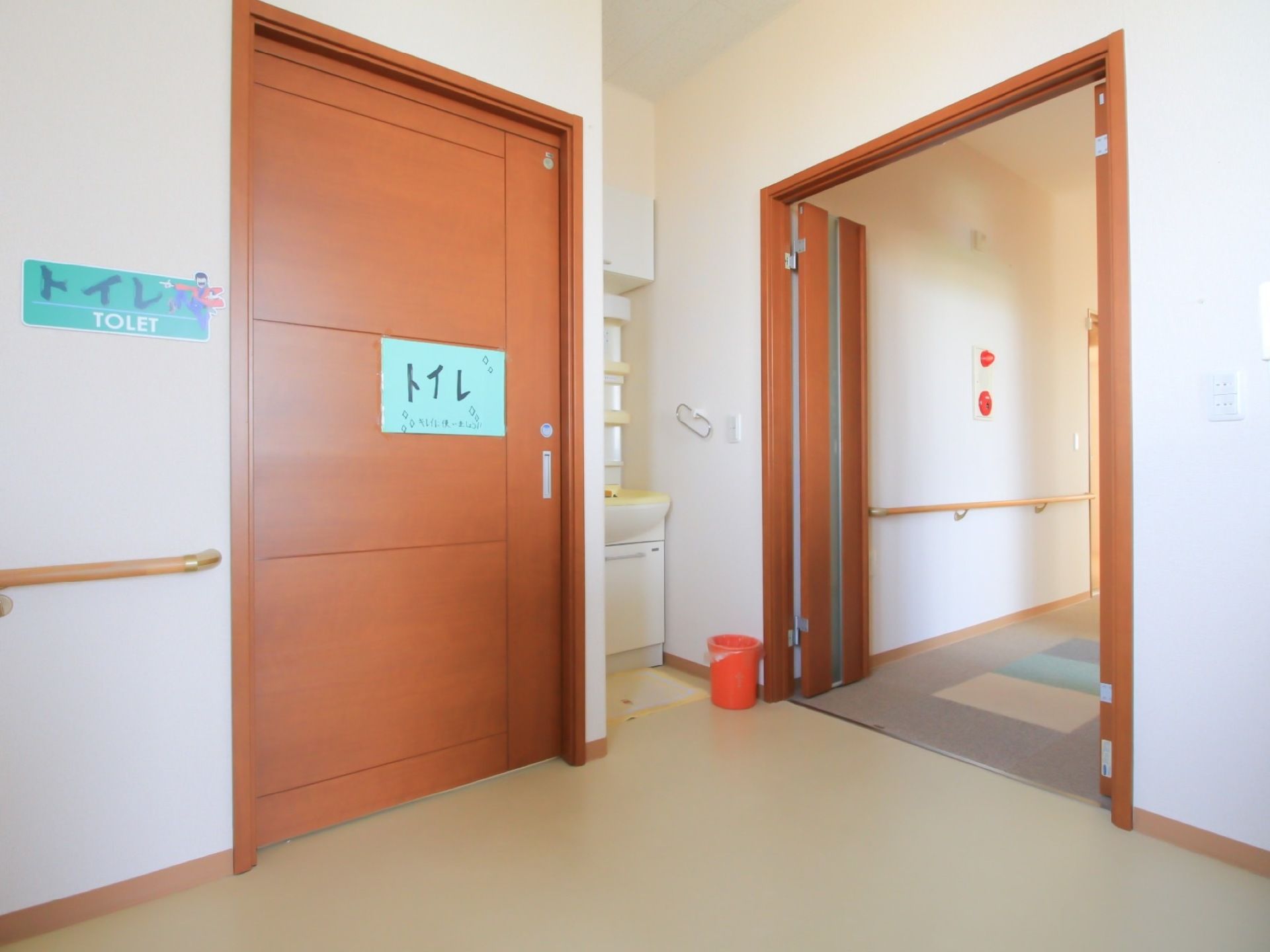 横幅の広いスライドドアがあり、トイレの表示がされている。壁には手すりが付いていて、洗面台が設置されている。