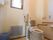 部屋の角に洋式トイレが設置されている。蓋付きの青いポリバケツが置いてあり、すりガラスの窓の外は明るい。