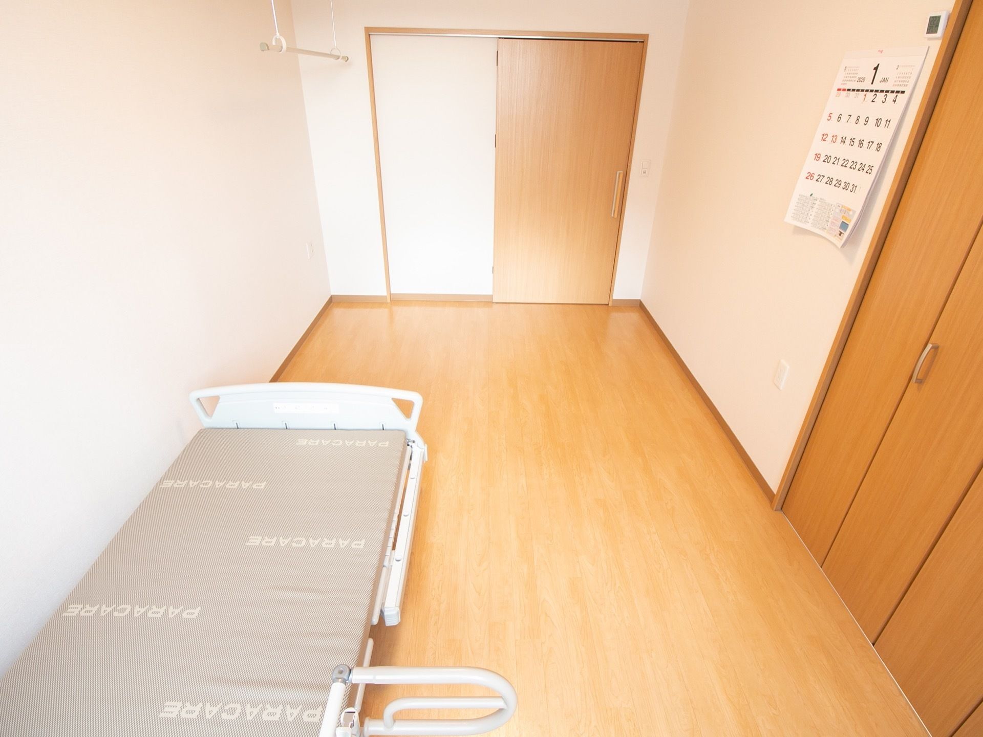 長方形の間取りの居室で、床はフローリング。壁紙は白色である。介護ベッドが設置され、作り付けのクローゼットもある。