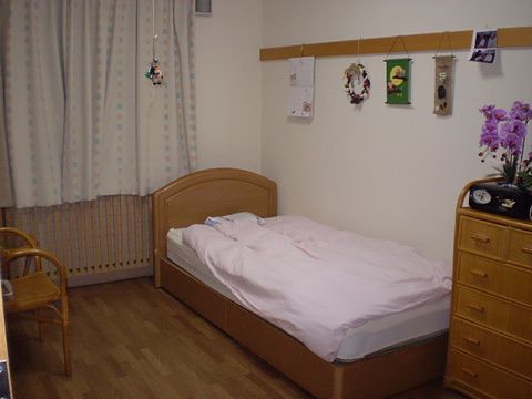 寝具付きのベッドが置かれたフローリングの部屋には、花の写真や花が飾られている。