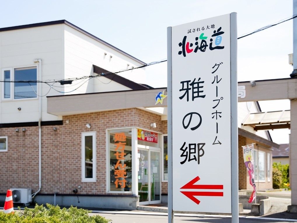 ホーム名が大きく黒い文字で書かれた看板には赤い矢印も添えられている。看板の後ろには処方箋を受け付ける薬局もあり、赤と黄色ののぼりも立っている。