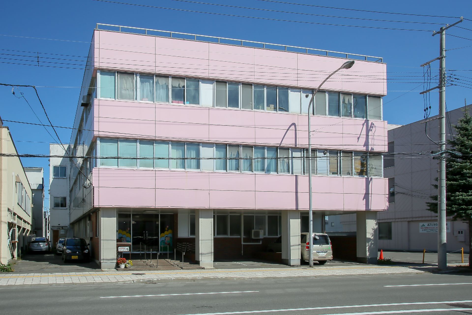 一階部分に駐車場とスロープ付き階段が玄関前にあるピンクの外壁の建物