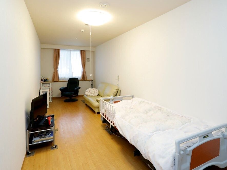 フローリングの部屋には寝具付きのベッドが置かれ、カーテンとカーテンが付いた大きな窓があり、ソファやテレビもある。