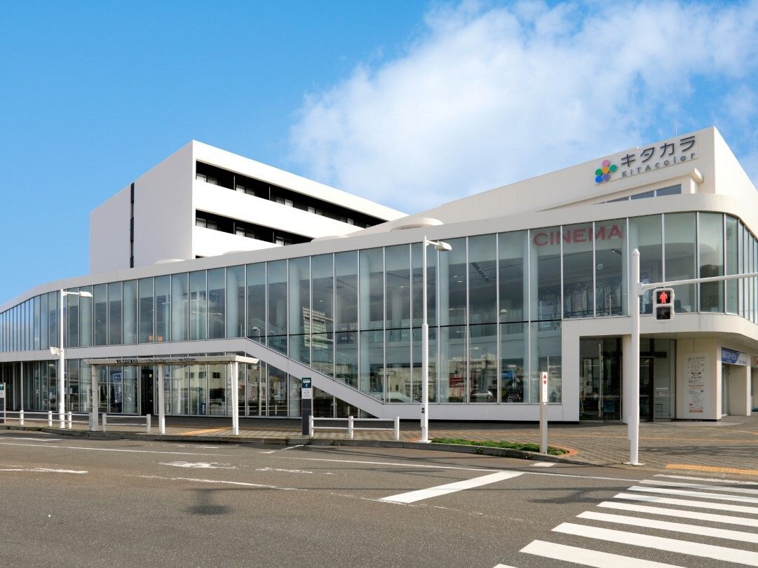 青い空の下に建っている白を基調とした大きな建物。目の前には横断歩道の付いた道路がある。