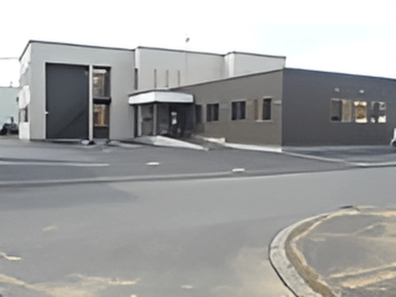 広い駐車場が付いた建物は白と黒でまとめられていて、目の前には道路もある。日当たりのいい場所に建っている。