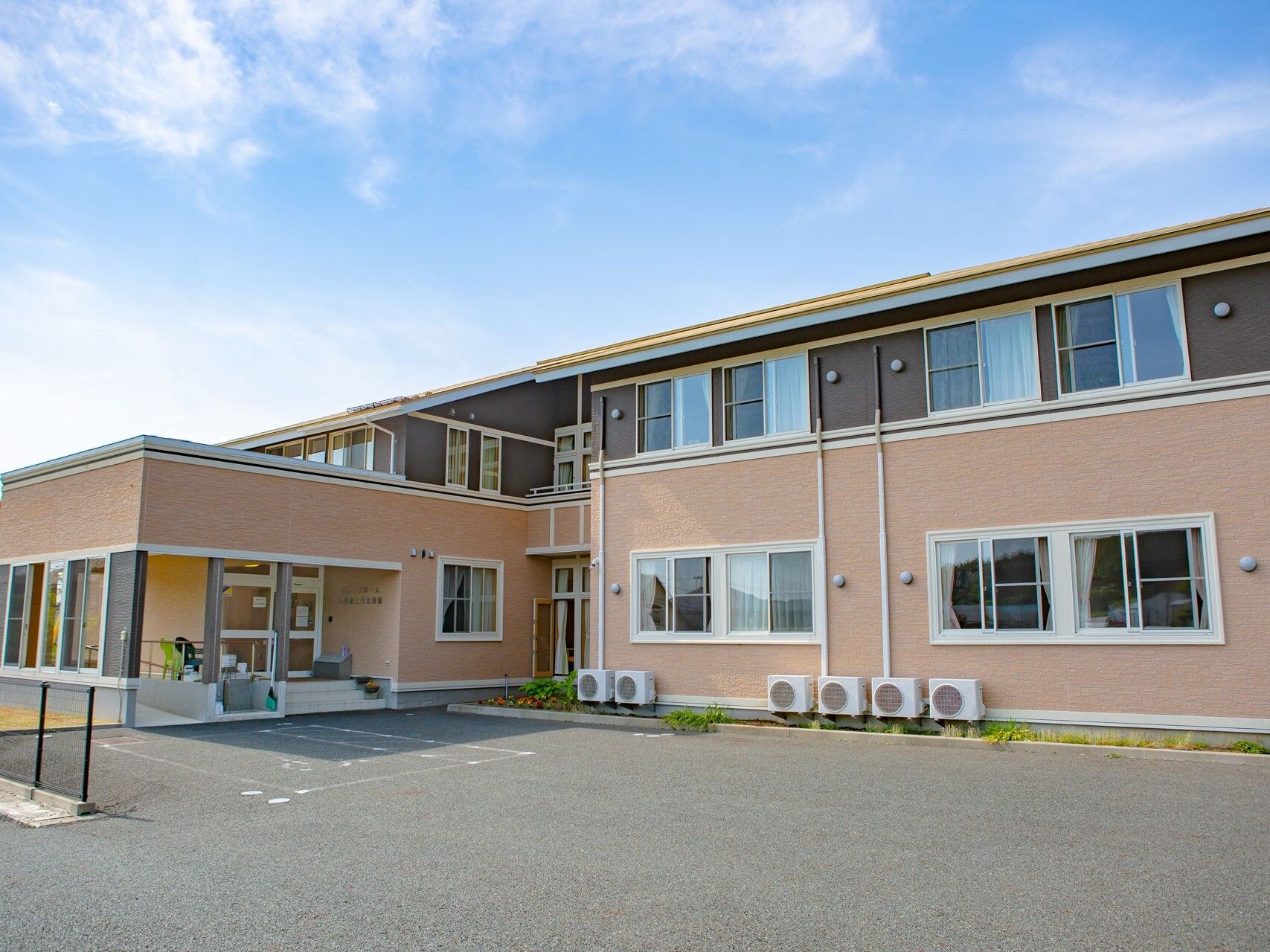 ブラウン系の外観の２階建ての建物は日当たり良好で横に長く、2階部分には一部ベランダがある。