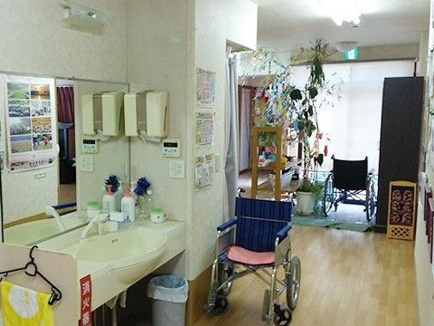 洗面所にはハンドソープやごみ箱、ハンガーにかけられたタオルなどがあり、車いすも近くにある。奥には七夕飾りが見える。