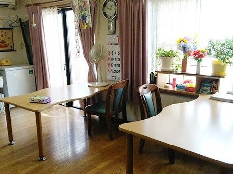 波型のテーブルが二つ並び、テーブルの上には扇風機が、棚の上には花が飾られている。