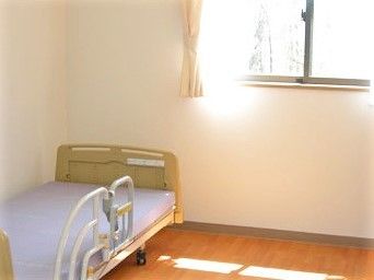 小さなベッドが置いてある窓付きのワンルーム。施設内の居室の写真