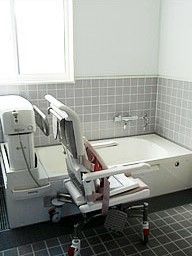 座った姿勢を保てるリフト付きの介護式浴槽。安全を保つための施設内の装置の写真