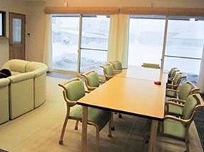 長机が一つと椅子が多数並ぶリビング。左側にソファがあるダイニングスペース