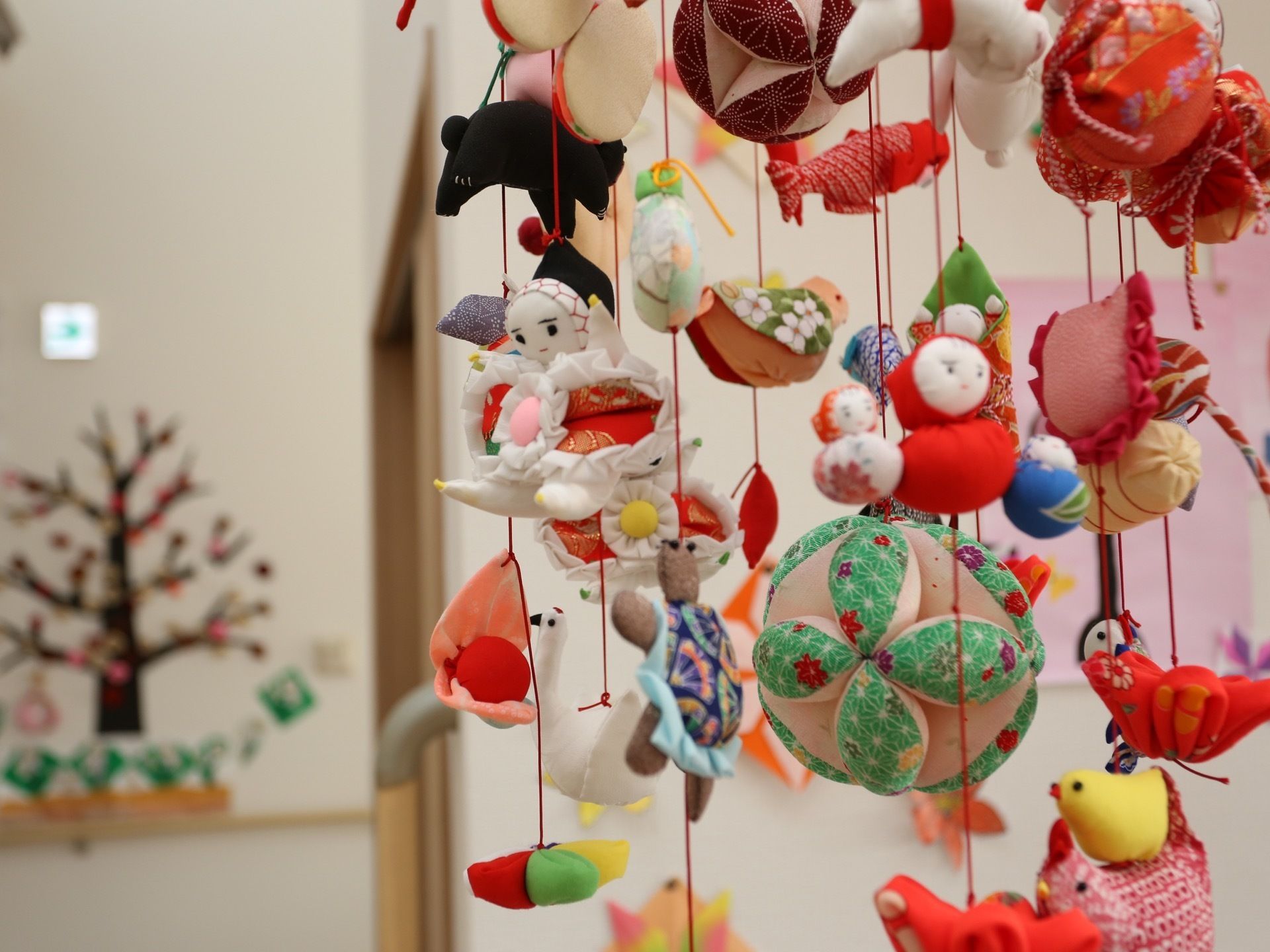 館内に飾られた雛飾りの画像である。ちりめんの生地で作られたひよこや魚などの飾りが赤いひもで繋がれている。