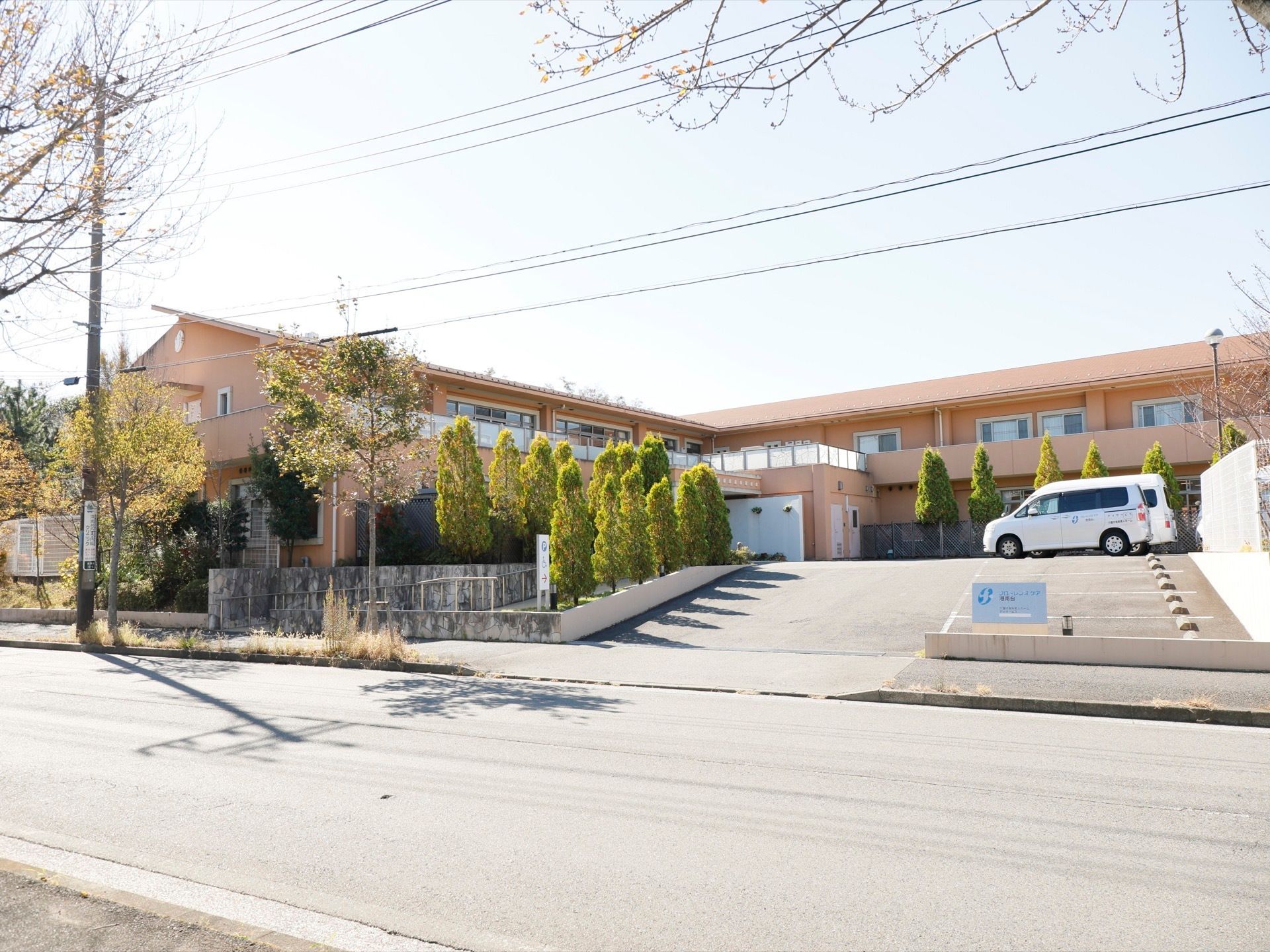 施設は2階建てで柔らかなオレンジ色の外壁となっている。駐車場が完備されている。周囲は木が植えられている。