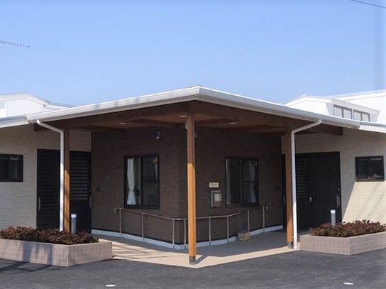 花壇や手すりが設置された玄関には屋根が付き、両サイドにドアが付いている。平屋建ての建物。