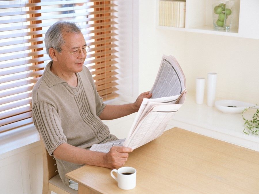 コーヒーを片手に新聞を読んでいるメガネをかけたご高齢の男性