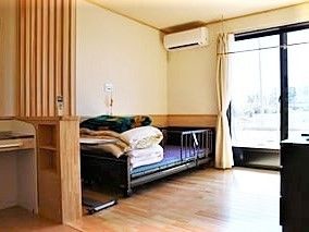 フローリングの居室。カーテン付きの窓とエアコン、ベッドがあり、車いす対応の洗面所もついている。