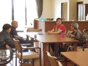 木製のダイニングテーブルが複数並んだ食堂。スタッフと数名の入居者が穏やかに過ごしている。