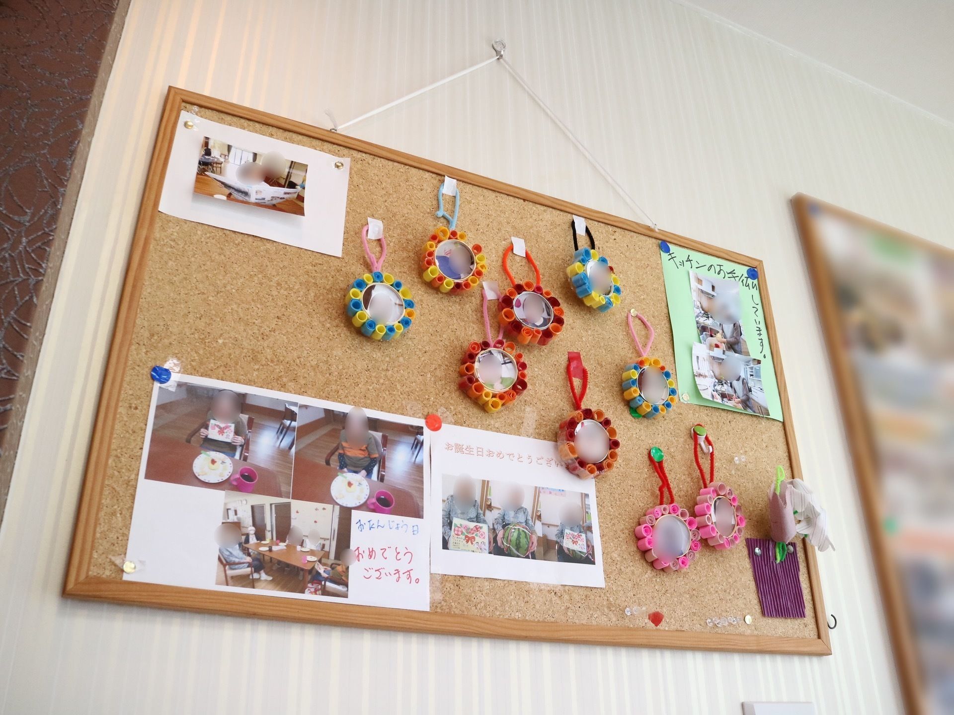 白い壁に大きなコルクボードが貼られている。誕生日を迎えた入居者様の写真や、さまざまな色の飾り付けがぶら下がっている。