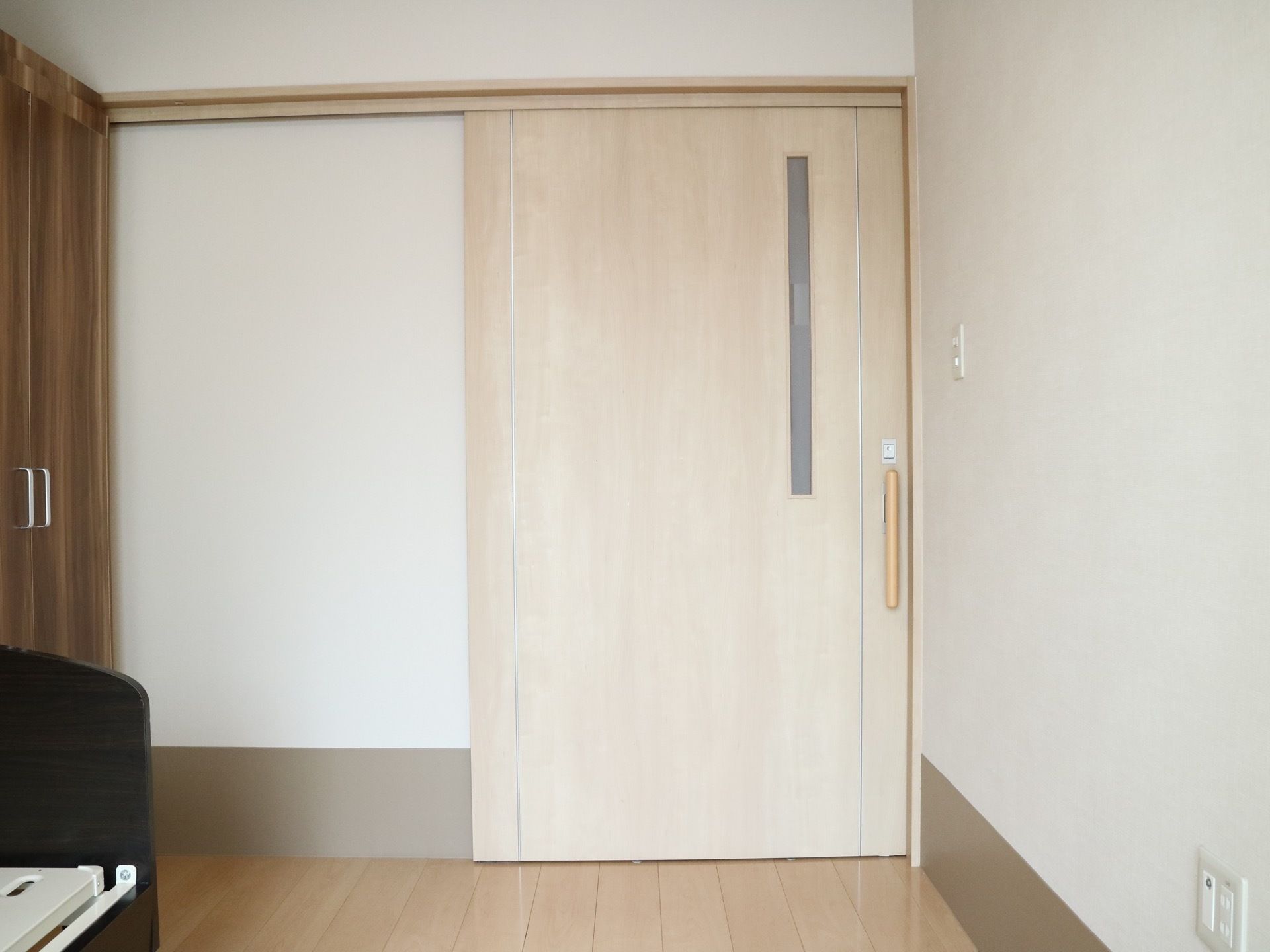居室のドアは大きな白い引き戸になっている。右側の壁には電気のスイッチがあり、左側には木目調のクローゼットが設置されている。