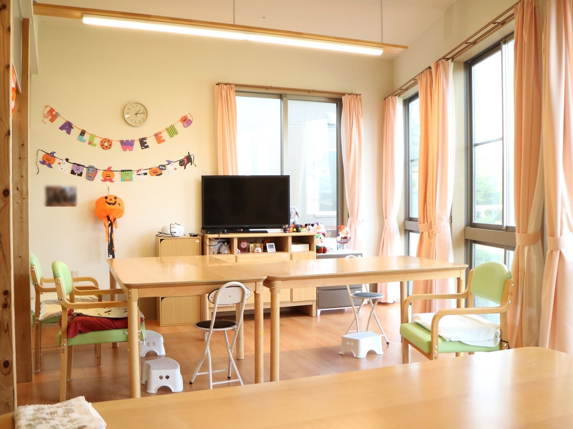 窓の多い明るい食堂である。テーブルや椅子、テレビなどが設置されており、壁にはハロウィンの飾り付けがされている。