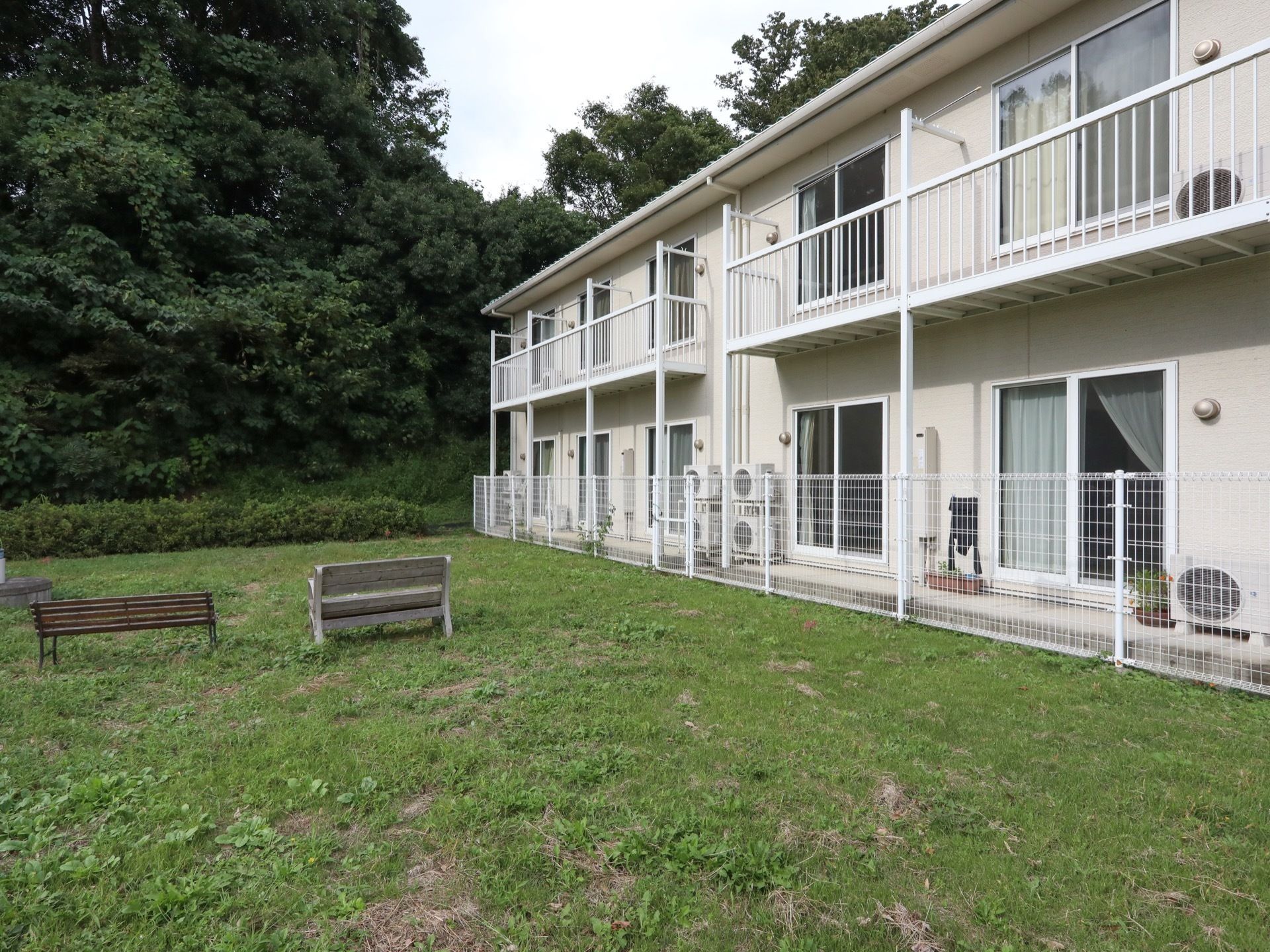 建物の側に広々とした庭がり、ベンチが２台置かれている。奥には木々が生い茂っており、緑の多い環境である。
