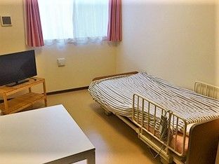 一人用のベッドとテレビ、テーブルが置いてある施設内の小さなワンルームの様子