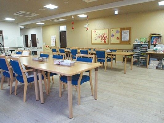 ブルーの椅子がセットされた木製のテーブルが複数あり、利用者の作品が壁に飾られている。