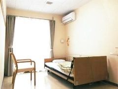 椅子と介護用ベッドが置いてある施設内の居室の様子。エアコンがついた小さな部屋