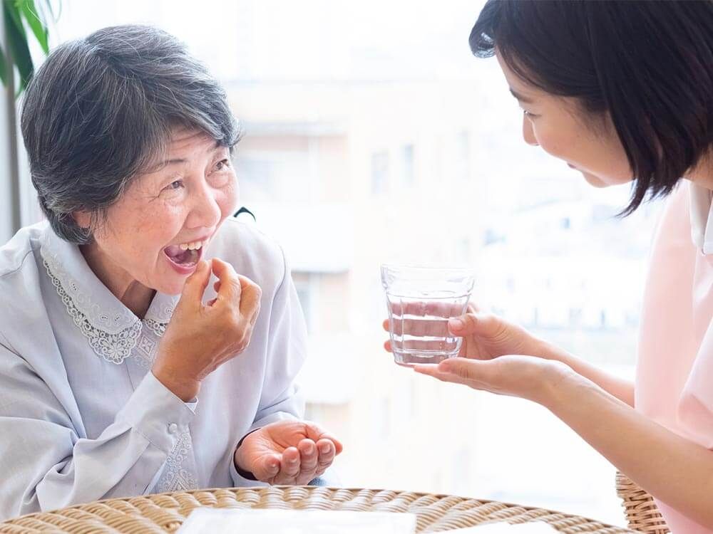 薬を飲む高齢女性と付き添いの女性ヘルパー