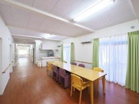 白い壁にモスグリーンのカーテンがかかった広めのホールの様子。長いテーブルと椅子が置いてある食堂のようなスペース