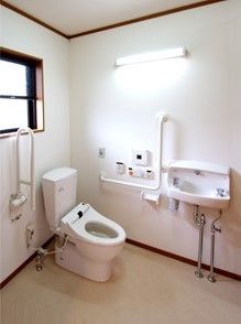 清潔なデザインのトイレと洗面台。L字型の手すりと可動式の手すりが付いている様子